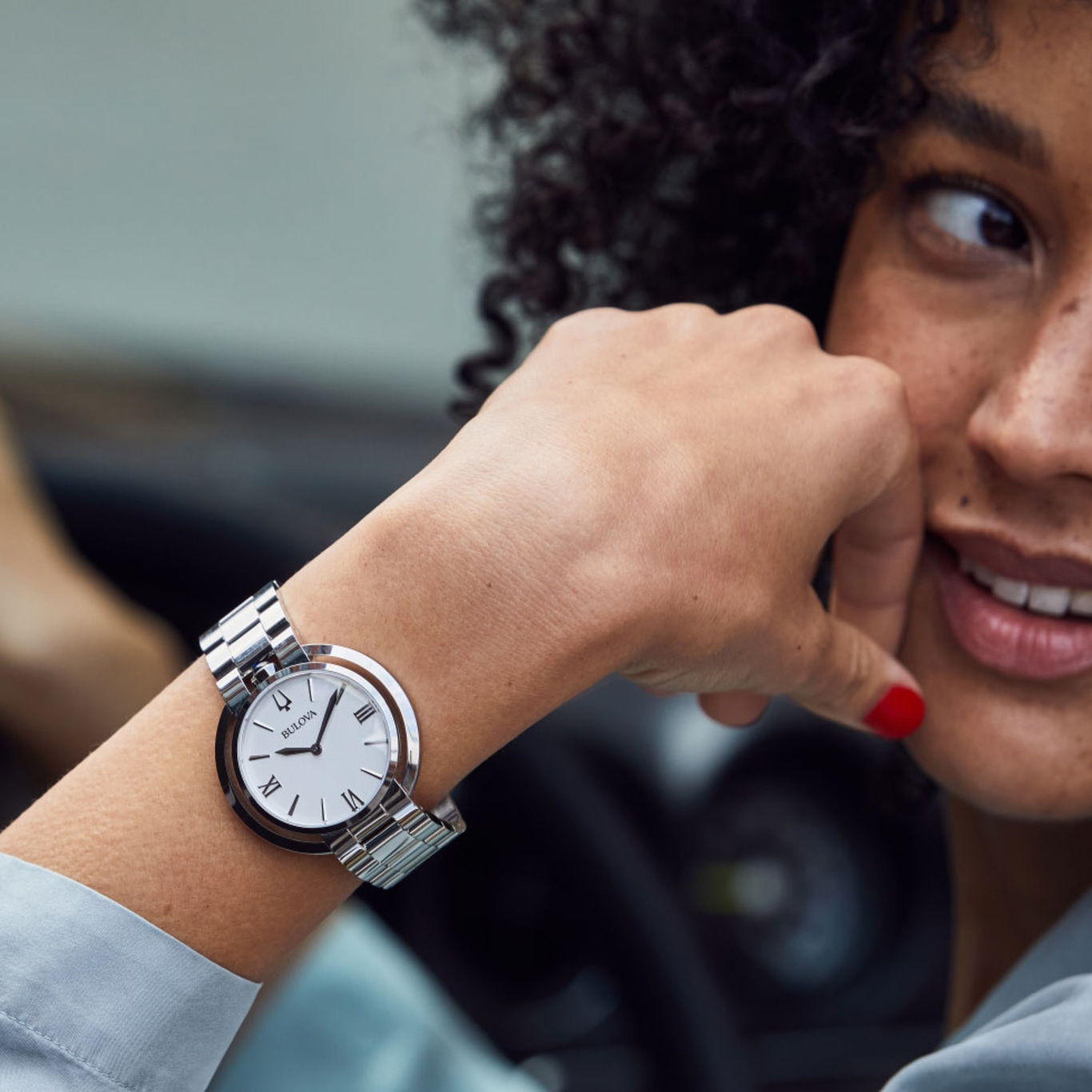Vrouw met horloge om haar pols, glimlachend en in de verte kijkend.