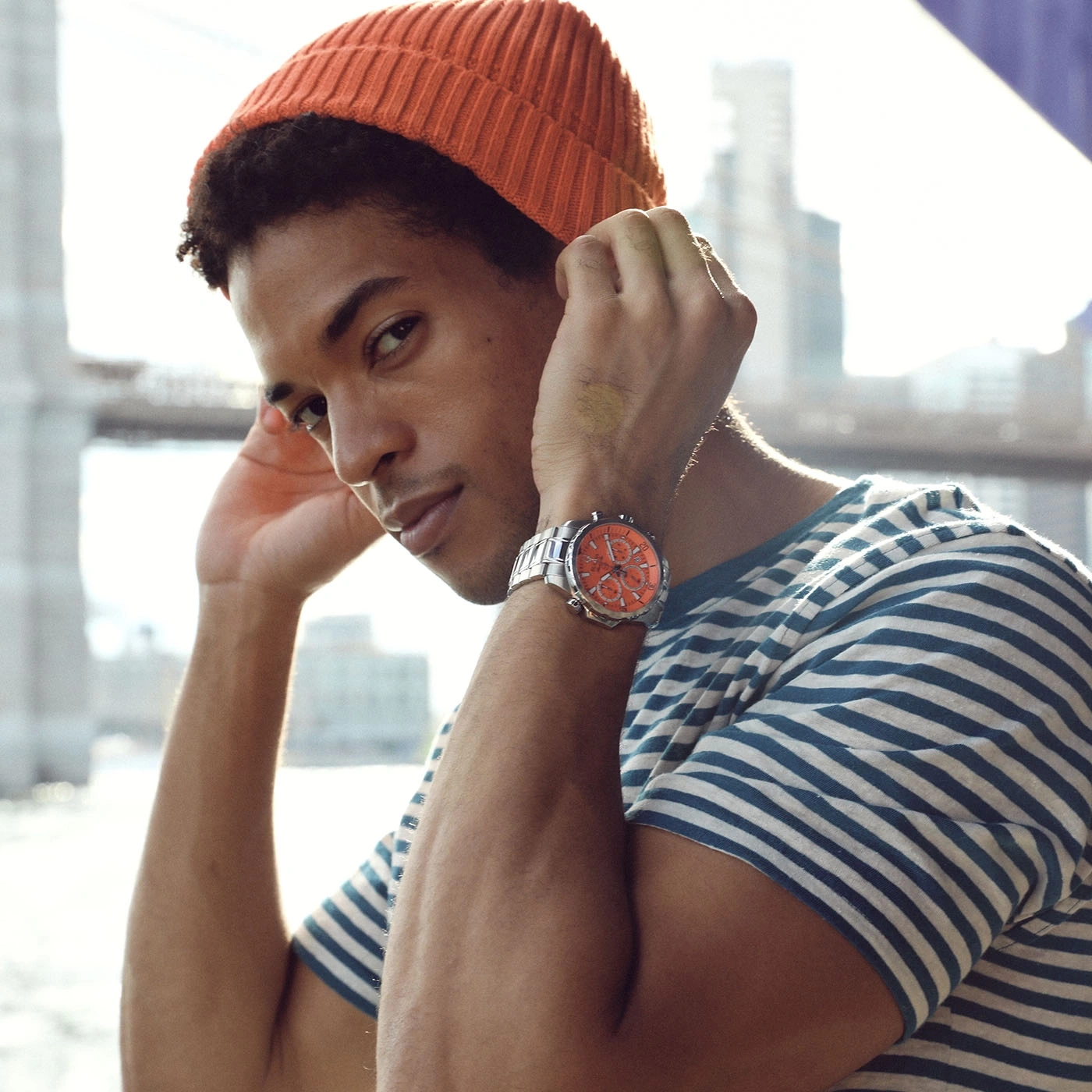 Man met oranje muts en horloge, gestreept t-shirt, kijkt in de camera, buiten