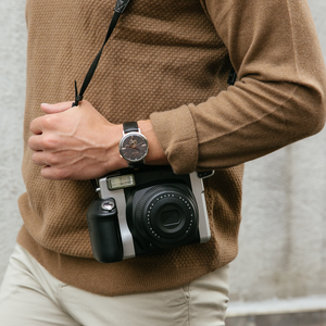 Man met horloge en camera, bruine trui, beige broek, close-up, mode