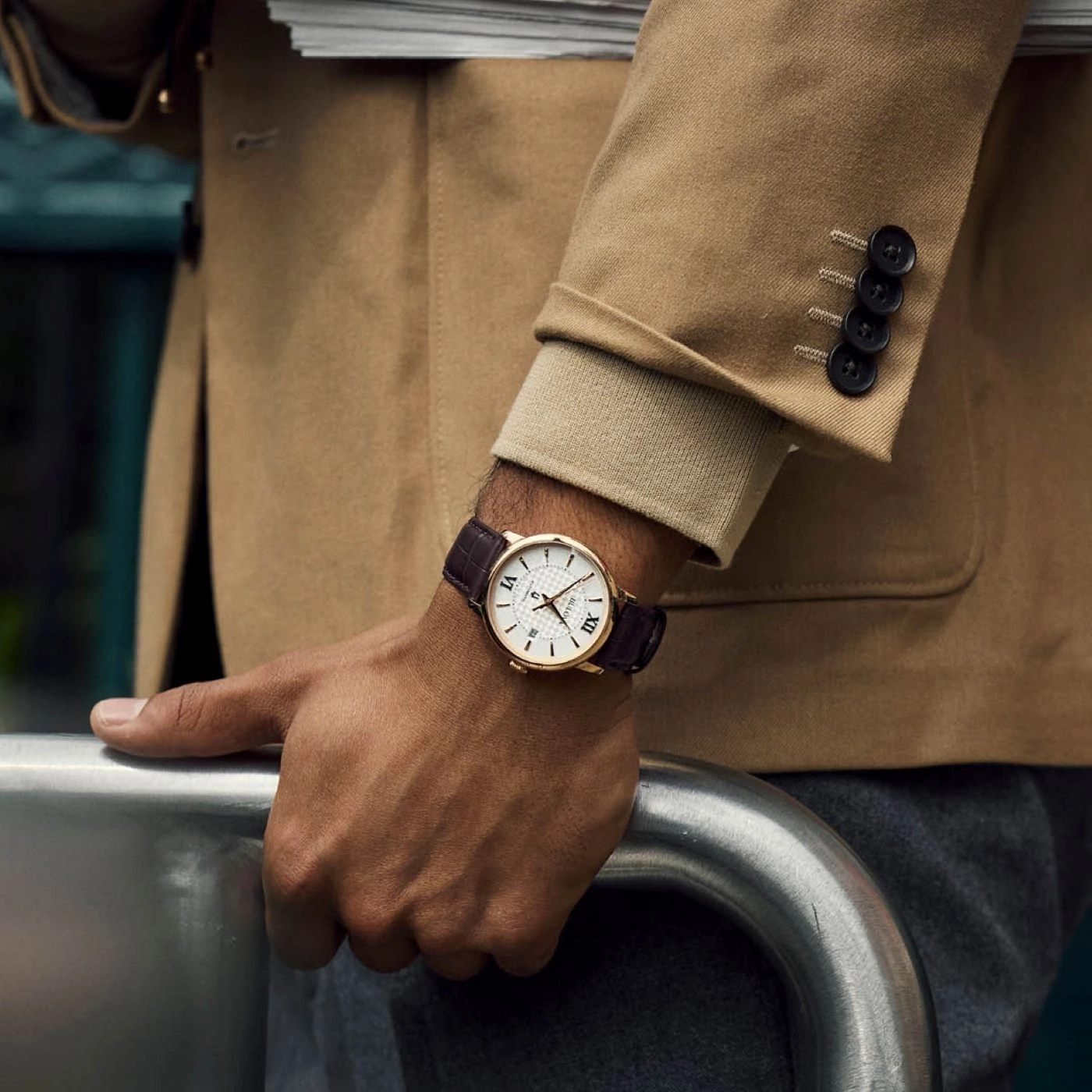 Man met horloge en jas die steunt op een metalen leuning.