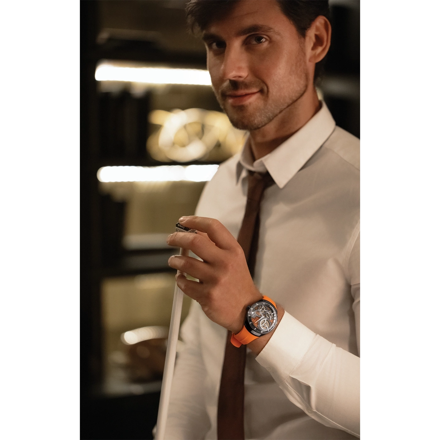 Man met horloge, overhemd en stropdas, houdt voorwerp vast, glimlacht