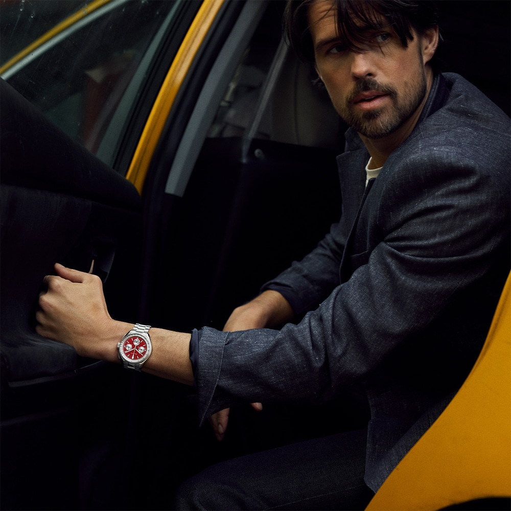 Man in taxi met horloge om pols. Zwarte jas en rode wijzerplaat.