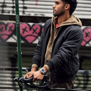 Man met fiets en horloge, voor graffiti-achtergrond, casual gekleed.