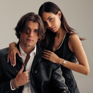 Een paar poseert met sieraden. Man in leren jas, vrouw in zwart. Gouden accessoires.