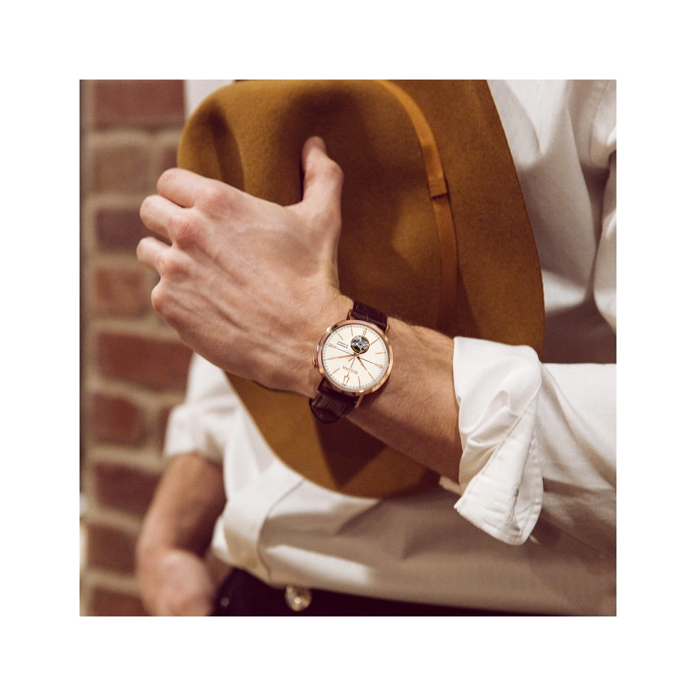 Man met horloge en hoed leunend tegen bakstenen muur