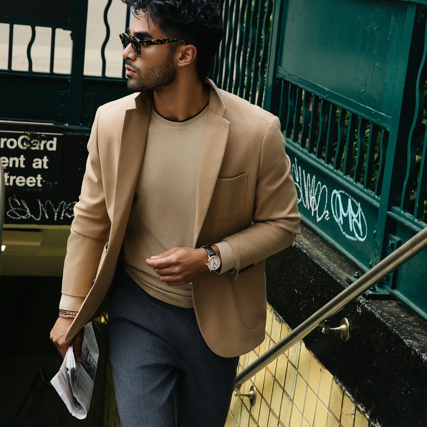 Een man in een blazer loopt een trap af met een krant in zijn hand.