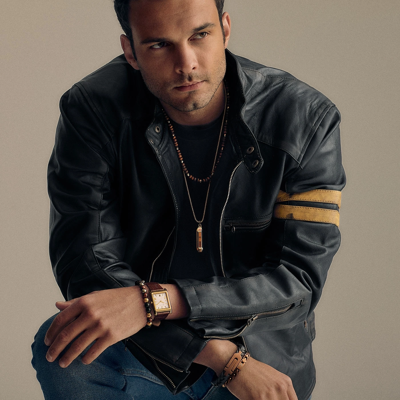 Man in leren jas met sieraden en horloge, jeans, poseert