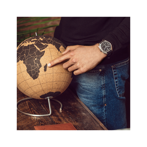 Man wijst naar globe, horloge om pols, jeans, houten oppervlak, close-up