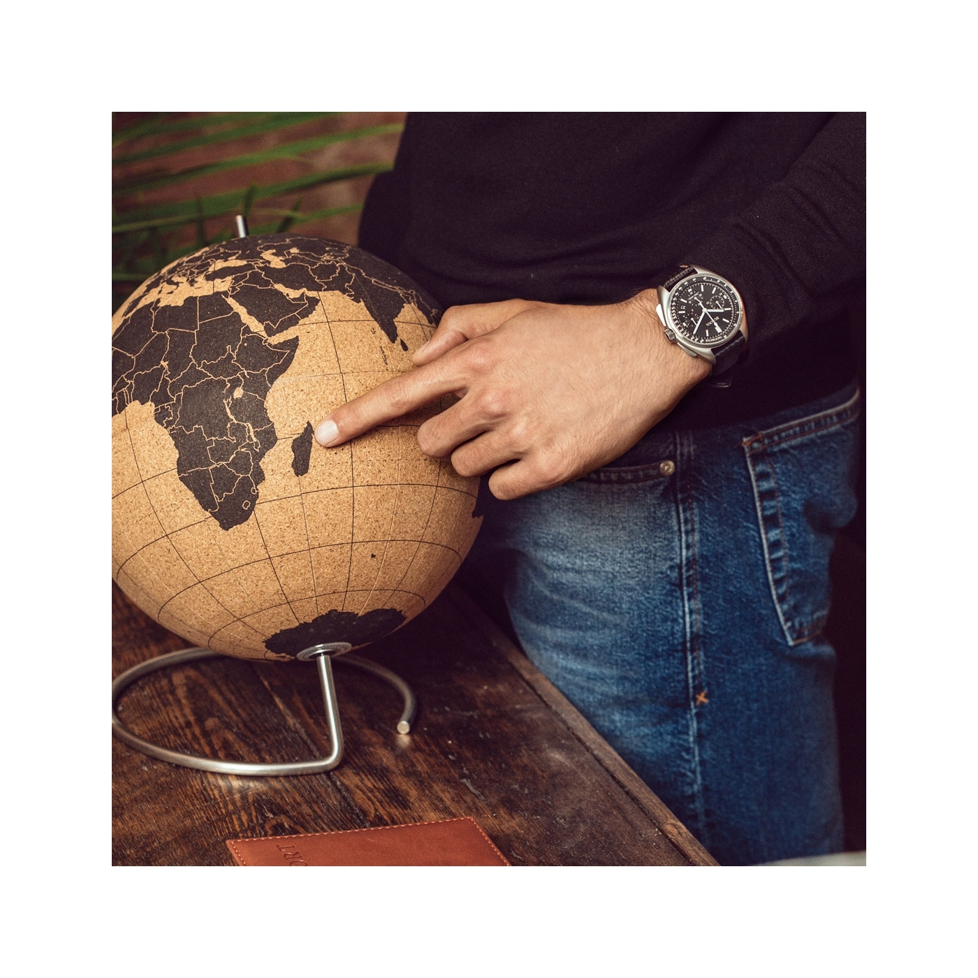 Man wijst naar globe, horloge om pols, jeans, houten oppervlak, close-up