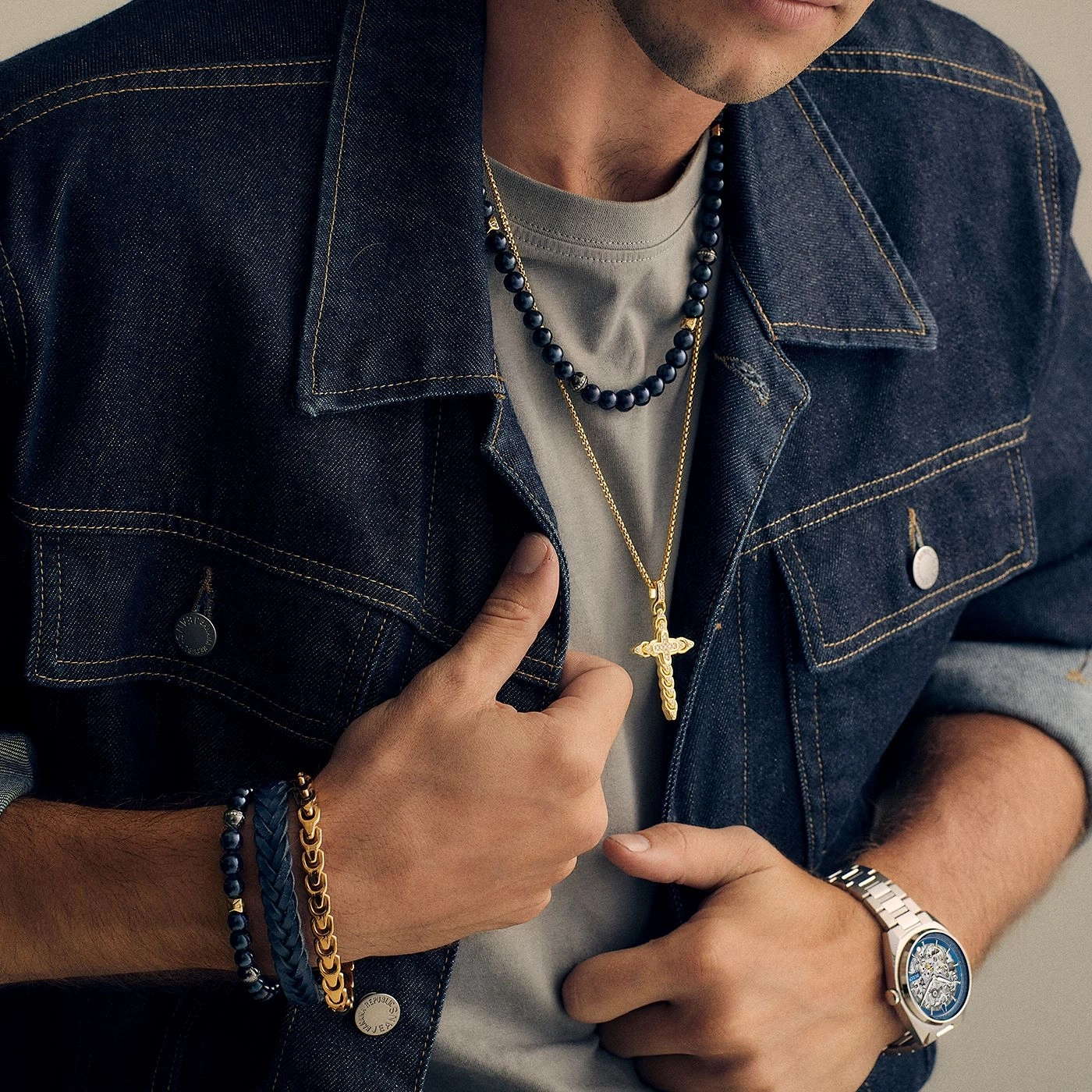 Man met sieraden, spijkerjas en horloge. Hij houdt zijn jas open.