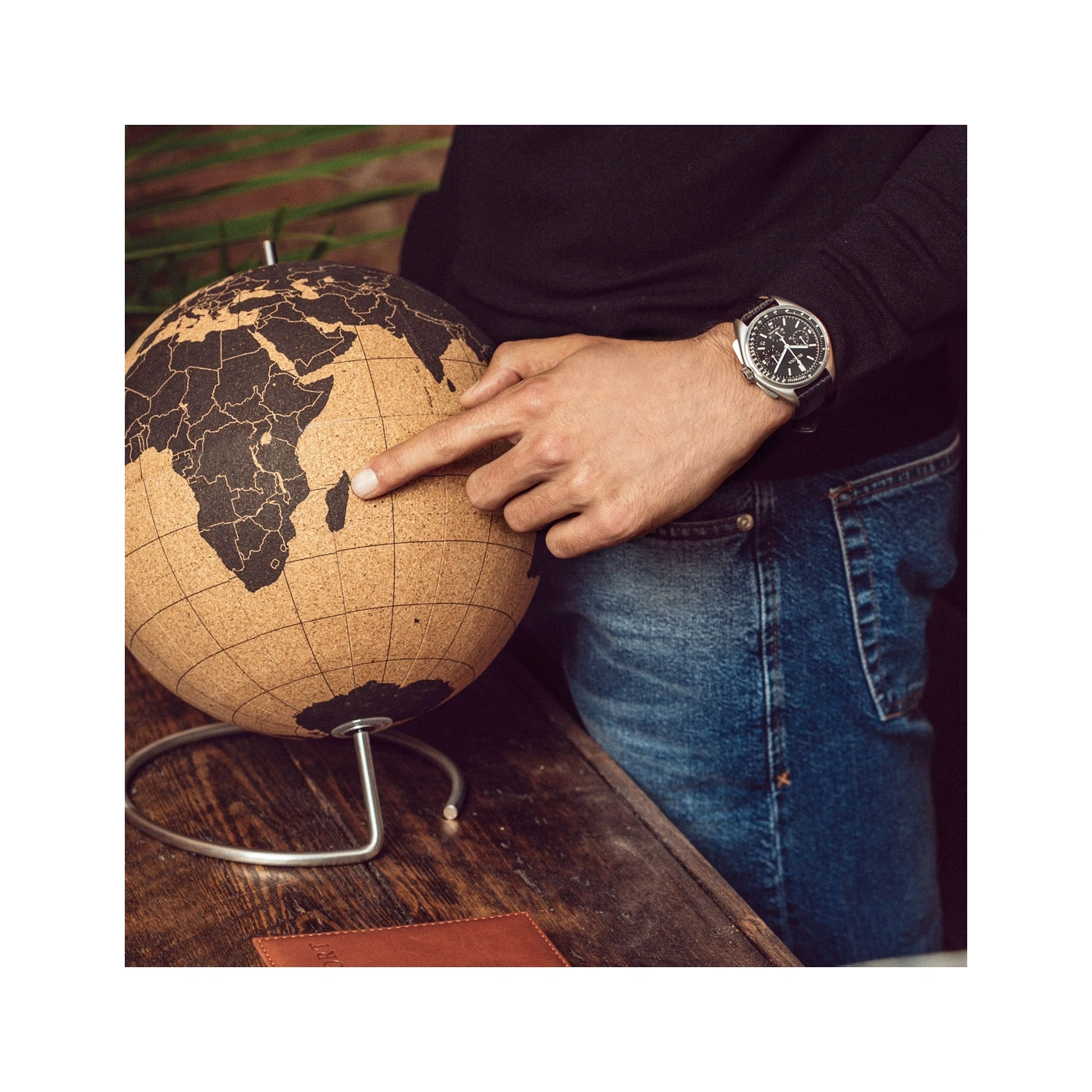 Man wijst naar Madagaskar op een wereldbol, draagt een horloge en spijkerbroek.
